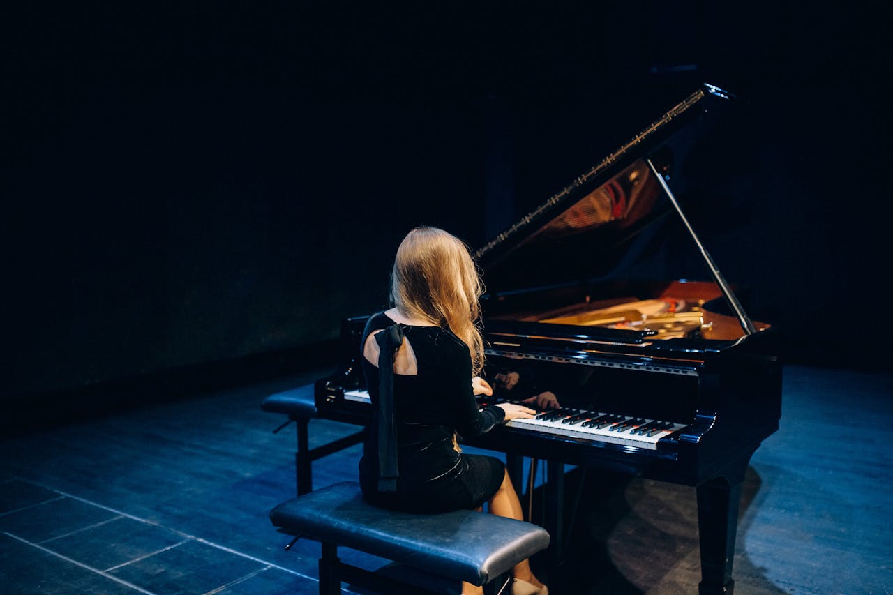 A female musician elegantly plays a grand piano on stage, creating a captivating musical experience.